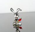May include: A glass rabbit figurine with a carrot in its mouth. The rabbit is clear glass with black eyes and white accents. The carrot is red and orange glass.