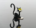 May include: Miniature black glass cat figurine with yellow eyes. The cat is sitting with its tail curled. The figurine is on a dark reflective surface with a coin next to it. The glass cat is a whimsical, handcrafted piece, perfect for collectors of unique glass art or animal figurines.