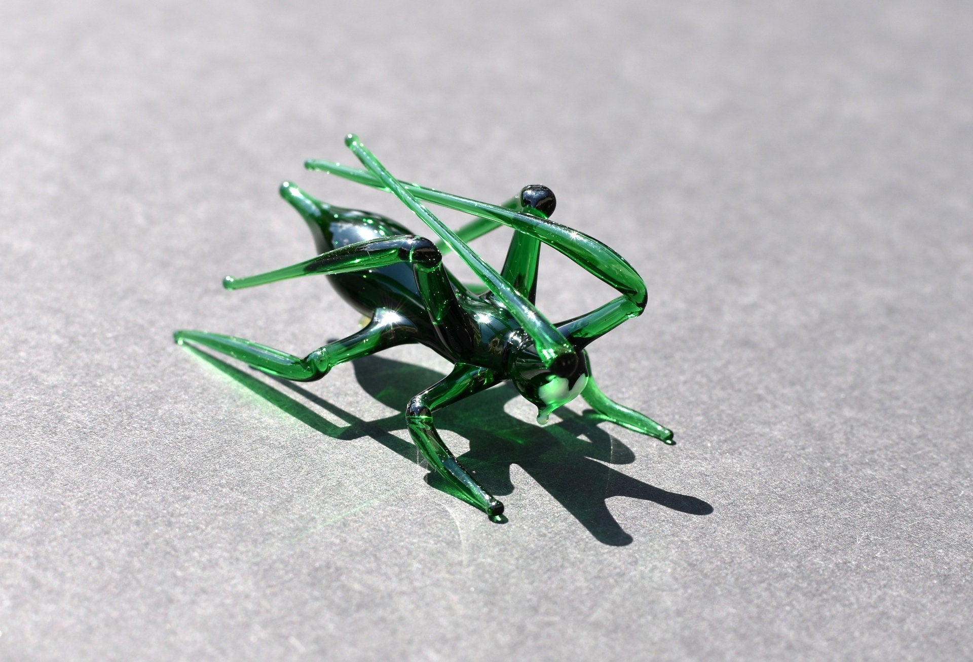 May include: A green glass grasshopper figurine with long legs and antennae.