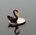 May include: A small black glass swan figurine with an orange beak sitting on a silver US quarter coin.