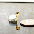 May include: A small glass turtle figurine with a white shell and gold accents. The turtle is standing on a reflective surface with a silver coin behind it.