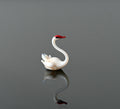May include: A small white glass swan figurine with a red beak. The swan is in a swimming pose with its head turned to the side.