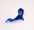 May include: A small blue glass figurine of a seal with white and black details. The seal is lying on its belly with its flippers outstretched.