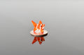 May include: A small orange and white glass fish figurine sitting on a silver coin.