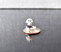 May include: A small, white glass figurine of a dalmatian dog sitting on a silver US quarter. The dog has black spots and is looking to the right. The figurine is sitting on a black surface.