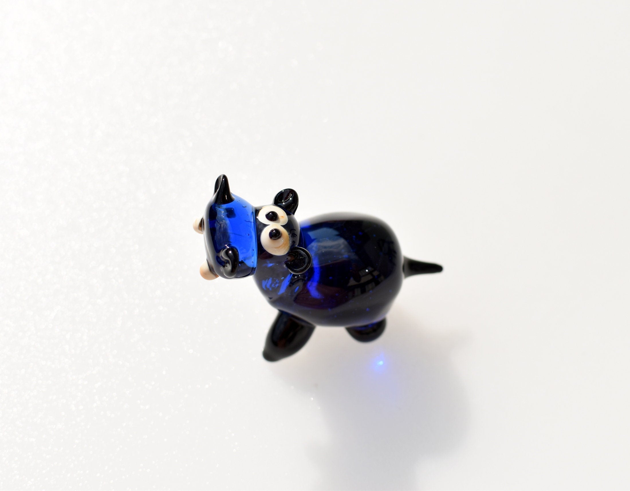 May include: A blue glass hippopotamus figurine with black eyes and a white background.