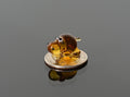 May include: A small amber glass figurine of a dog sitting on a silver coin. The dog has black eyes and a brown body.