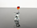 May include: A glass elephant figurine with a red and orange heart on its trunk.