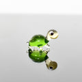 May include: A small glass turtle figurine with a green shell and a white head. The turtle is standing on a reflective surface and its reflection is visible below it.