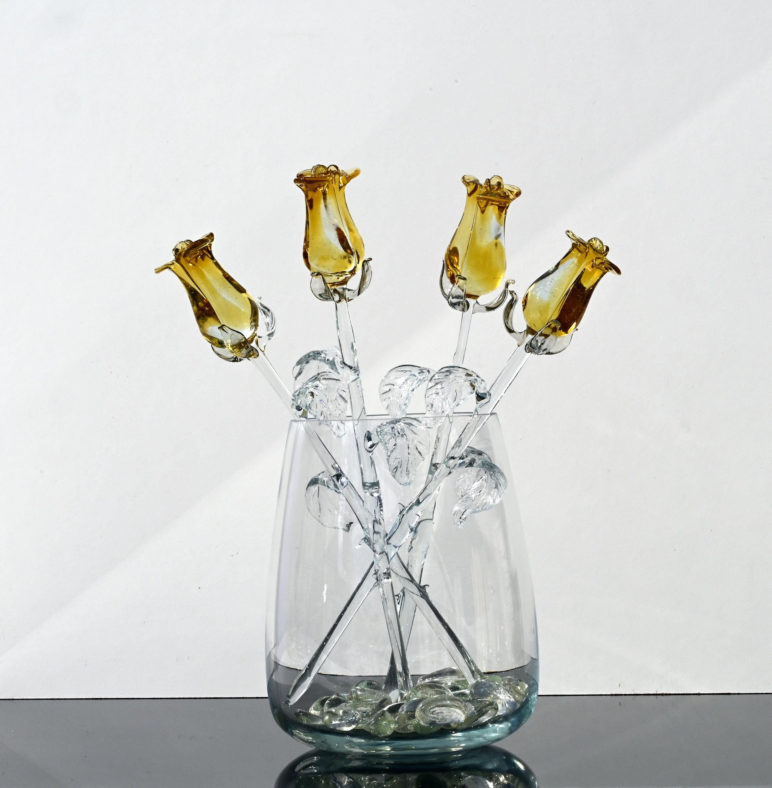 May include: A glass vase with five yellow glass roses. The roses are arranged in a bouquet and have clear glass stems and leaves.