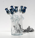 May include: A bouquet of six blue glass roses in a clear glass vase. The roses are arranged in a vase with clear glass stems. The roses are made of glass and have a blue tint. The vase is clear and has a round shape.