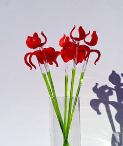 May include: A bouquet of red glass flowers with green stems in a clear glass vase.