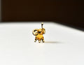 May include: A small, gold-colored glass elephant figurine with a raised trunk. The elephant is standing on a white surface.