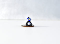 May include: A small blue and white glass penguin figurine sitting on a silver coin.
