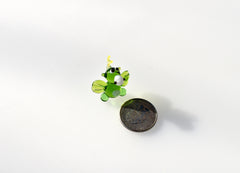May include: A small green glass figurine of a creature with a yellow party hat, white eyes, and white wings. The figurine is about the size of a US quarter.