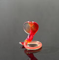 May include: A red glass snake figurine with a raised head and white eyes. The snake is coiled in a circle with its tail tucked under its body.
