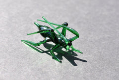 May include: A green glass grasshopper figurine with long legs and antennae.