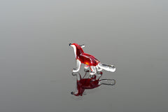 May include: A small glass figurine of a fox. The fox is red with a clear glass tail. The figurine is standing on a reflective surface.