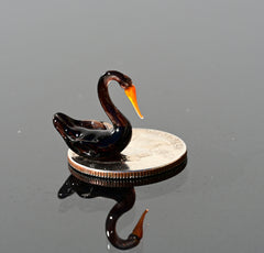 May include: A small black glass swan figurine with an orange beak sitting on a silver US quarter coin.