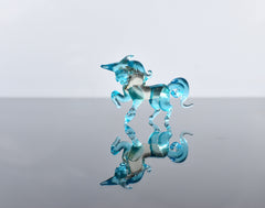May include: A glass unicorn figurine with a blue and white color scheme. The figurine is standing on a reflective surface.