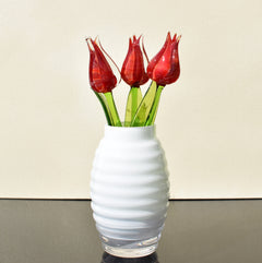 May include: Four red glass tulips with green stems in a white ribbed vase.