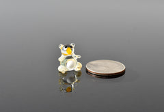 May include: A small, clear glass bear figurine with black eyes and a yellow nose. The figurine is sitting on a reflective surface and is next to a silver US quarter.
