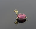 May include: A small glass turtle figurine with a pink shell and a yellow head and legs. The turtle has a white eye with a black pupil.