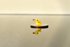 May include: A small yellow glass duck figurine with red eyes and a red beak sitting on a silver coin.