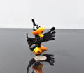May include: A small black glass bird figurine with orange beak and feet. The bird has large eyes and is in a startled pose with its wings spread out.