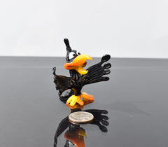 May include: A small black glass bird figurine with orange beak and feet. The bird has large eyes and is in a startled pose with its wings spread out.