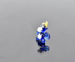 May include: A small blue glass figurine of a deer with a yellow antler. The deer has white eyes and a white belly. The figurine is standing on a reflective surface.