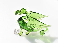 May include: A green glass dragon figurine with wings outstretched. The dragon has a long tail curled underneath its body. The dragon is about the size of a quarter.