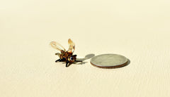 May include: A small glass bee figurine with brown and clear wings. The figurine is sitting on a beige surface next to a silver US quarter coin.