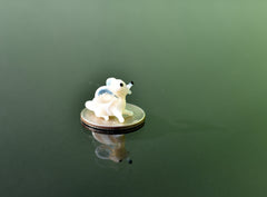 May include: A small white glass figurine of a mouse sitting on a silver US quarter coin.