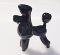 May include: A black ceramic poodle figurine with a shiny finish. The poodle is standing on all four legs with its tail curled up. The poodle's head is tilted to the side.