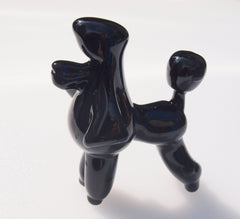 May include: A black ceramic poodle figurine with a shiny finish. The poodle is standing on all four legs with its tail curled up. The poodle's head is tilted to the side.