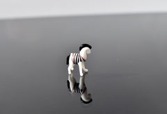 May include: A small glass zebra figurine with black and white stripes. The zebra is standing on a reflective surface and is facing to the right.
