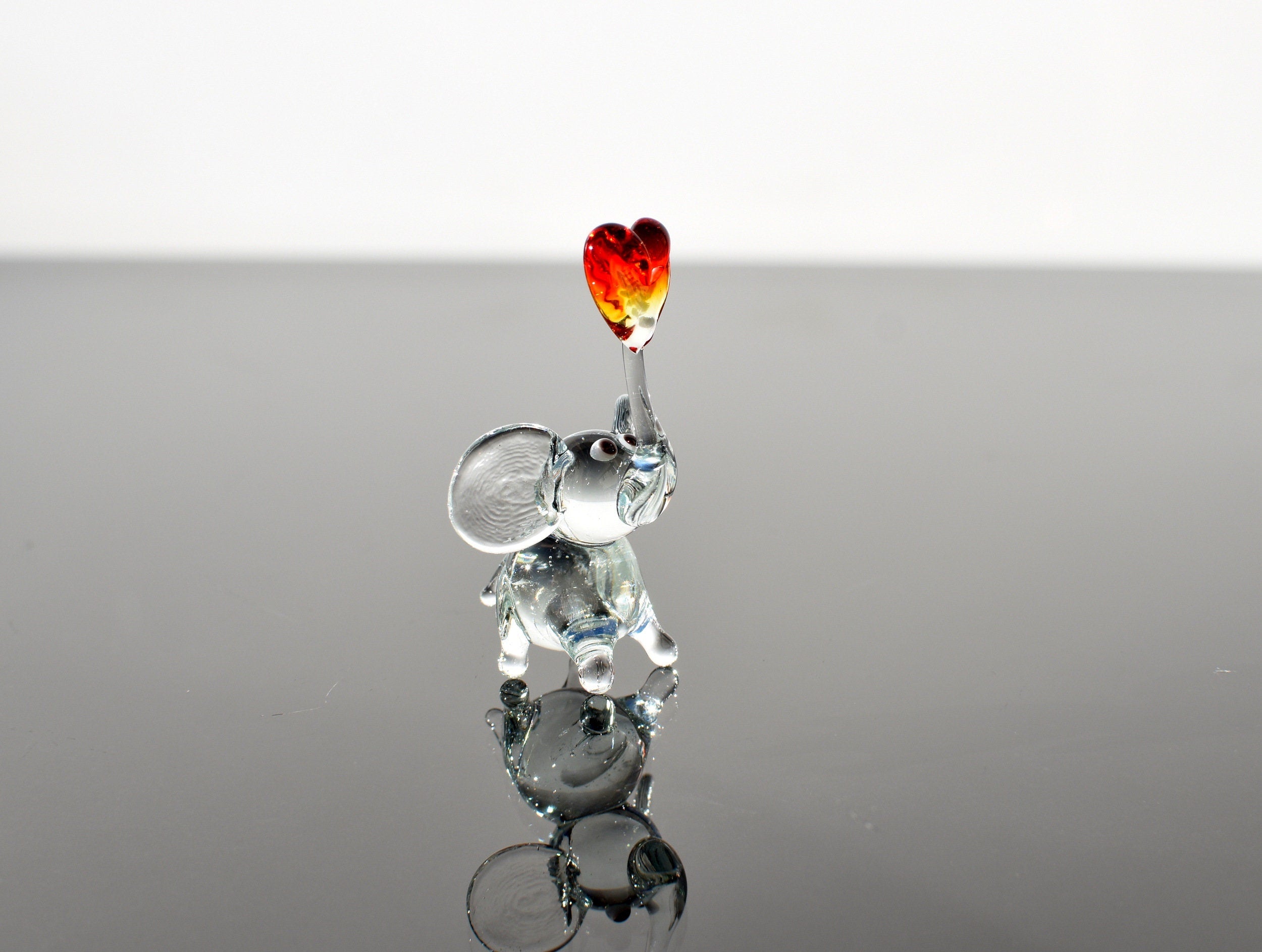 May include: A glass elephant figurine with a red and orange heart on its trunk.