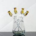 May include: A glass vase with five yellow glass roses. The roses are arranged in a bouquet and have clear glass stems and leaves.