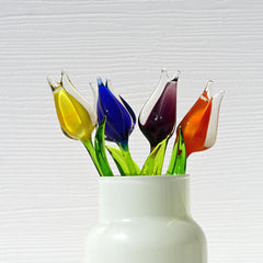 May include: Five glass tulips in a white vase.  The tulips are vibrant colors: yellow, blue, purple, and orange. The stems are green glass. The tulips are artfully arranged in a simple, elegant white vase.  These handcrafted glass flowers are a unique home decor accent.
