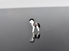May include: A small glass zebra figurine with black and white stripes. The figurine is standing on a reflective surface.