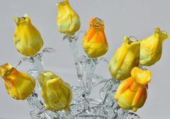 May include: A bouquet of glass flowers in shades of yellow and orange. The flowers are arranged in a clear glass vase. The flowers are made of blown glass and have a realistic appearance.