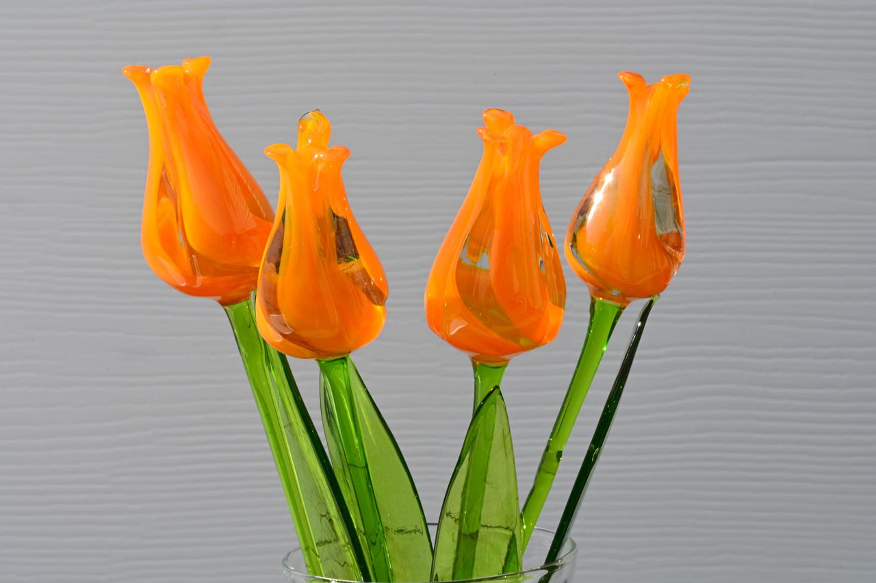 May include: Five orange glass tulips with green stems in a clear glass vase.