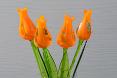 May include: Five orange glass tulips with green stems in a clear glass vase.