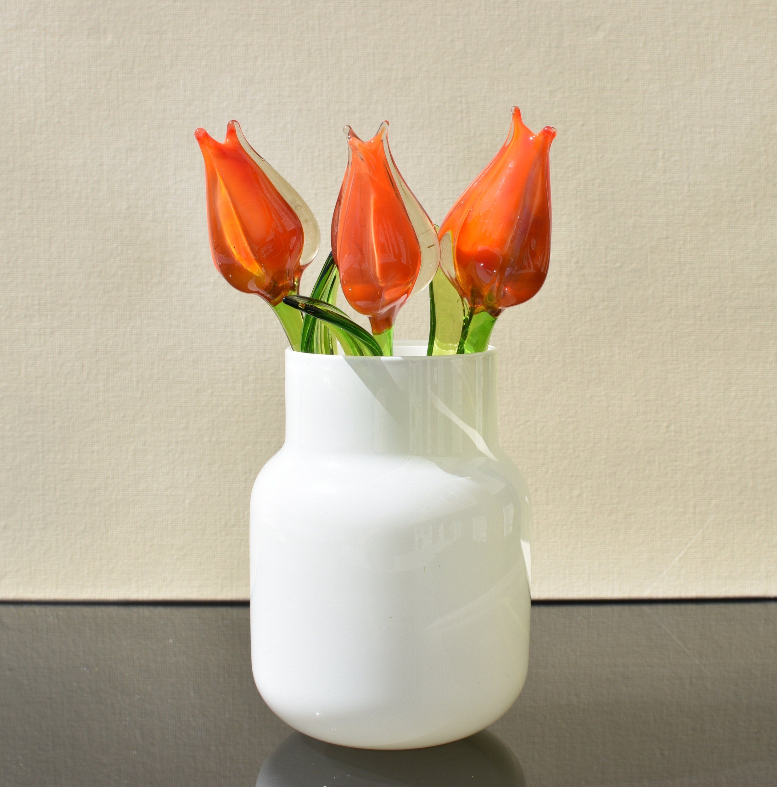 May include: Four orange glass tulips in a white ceramic vase